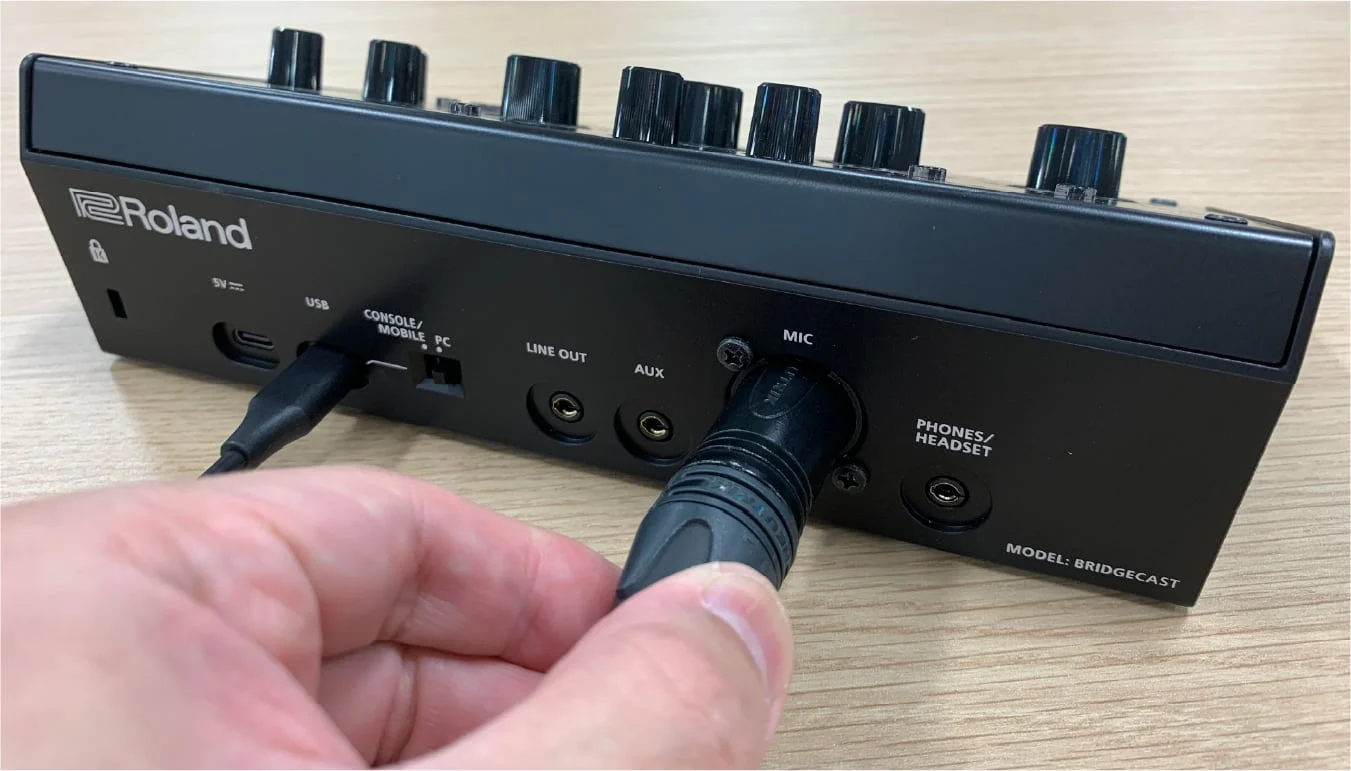 A person plugging in a microphone into the back of a Roland Bridge Cast mixer